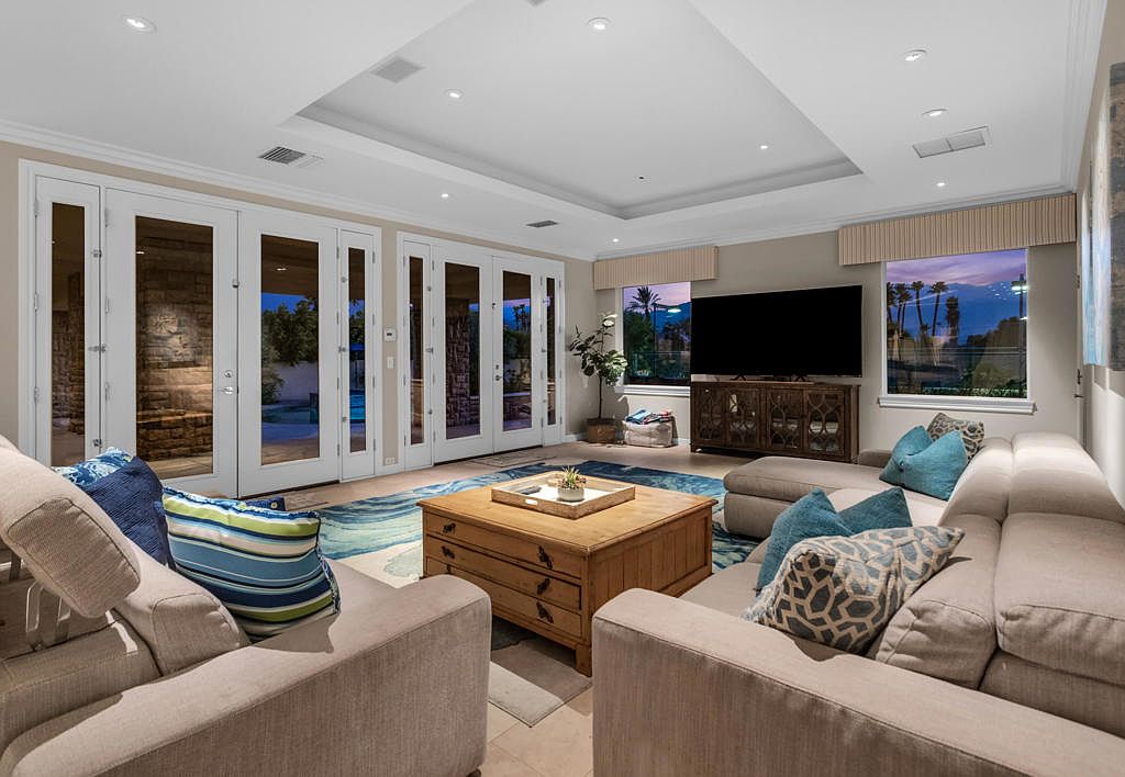 The great room — vaulted beamed ceiling, fireplace, and French doors opening to the pool and mountains beyond