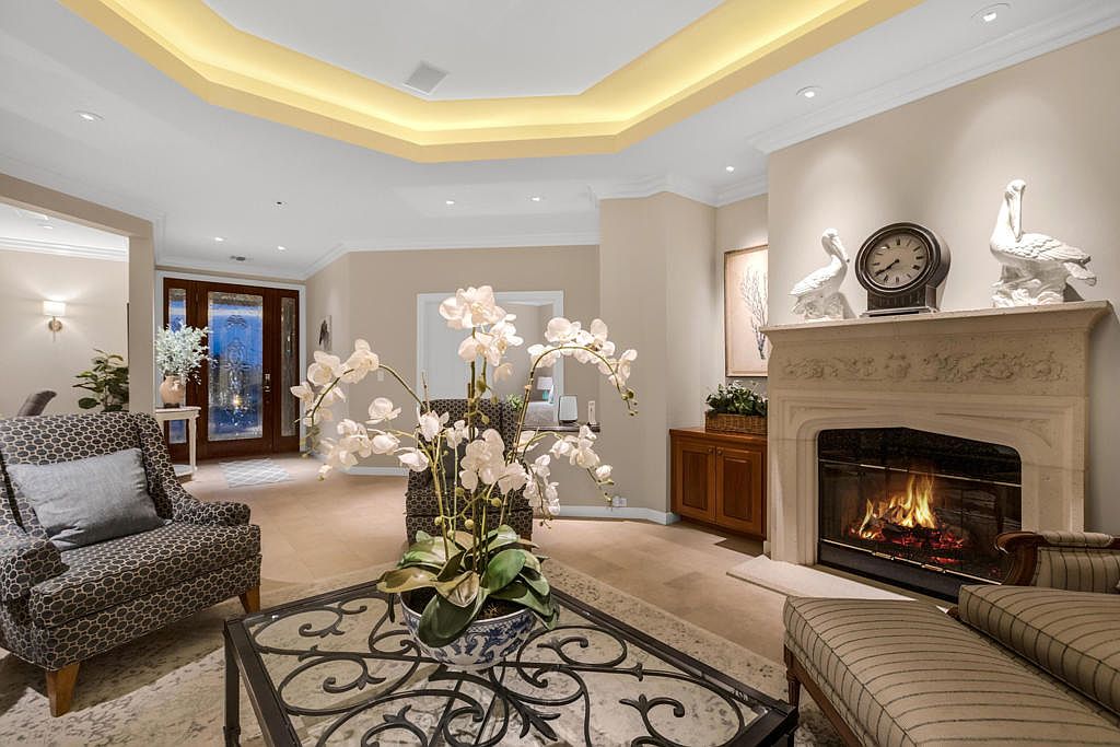 The foyer with a single orchid on a console table, fireplace illuminated, ambient ceiling cove